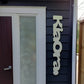 Decorative wooden nameplate on a house exterior with a door and window.