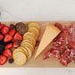 Wooden charcuterie board with meats, cheeses, fruits, and crackers on a white marble surface.