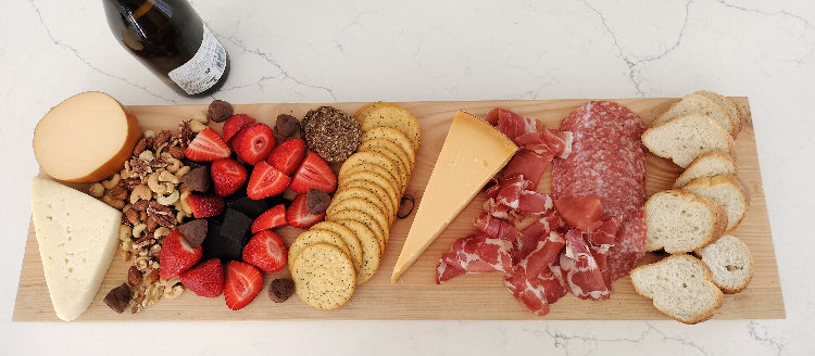 Wooden charcuterie board with meats, cheeses, fruits, and crackers on a white marble surface.