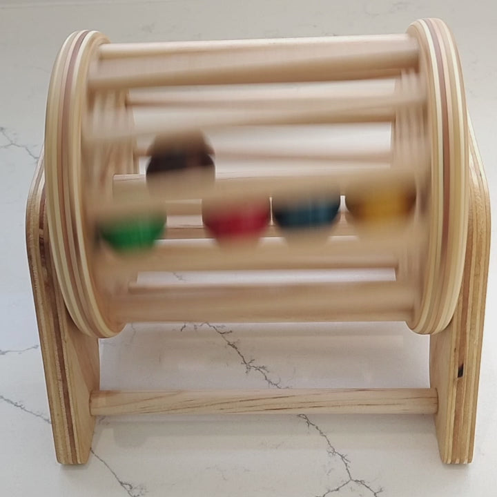 Wooden ball tumbler drum being spun with five coloured balls tumbling inside.